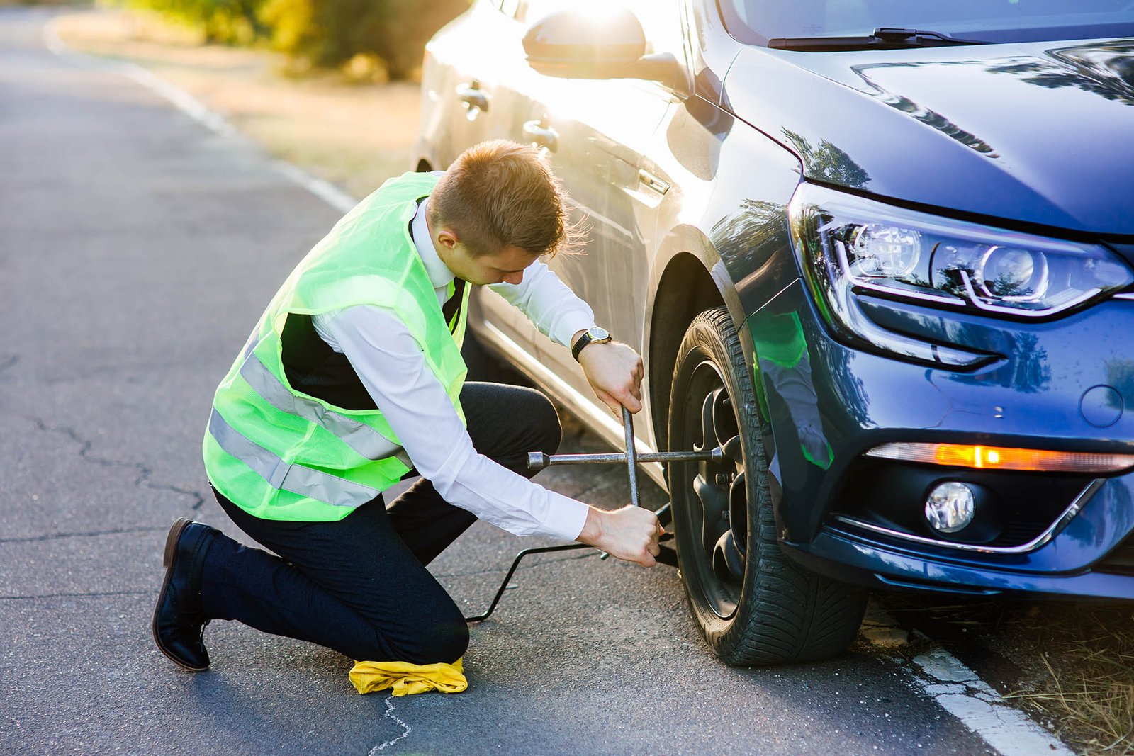 man in a green safety vest changes wheels on a car. Roadside tire change assistance service in Edmonton